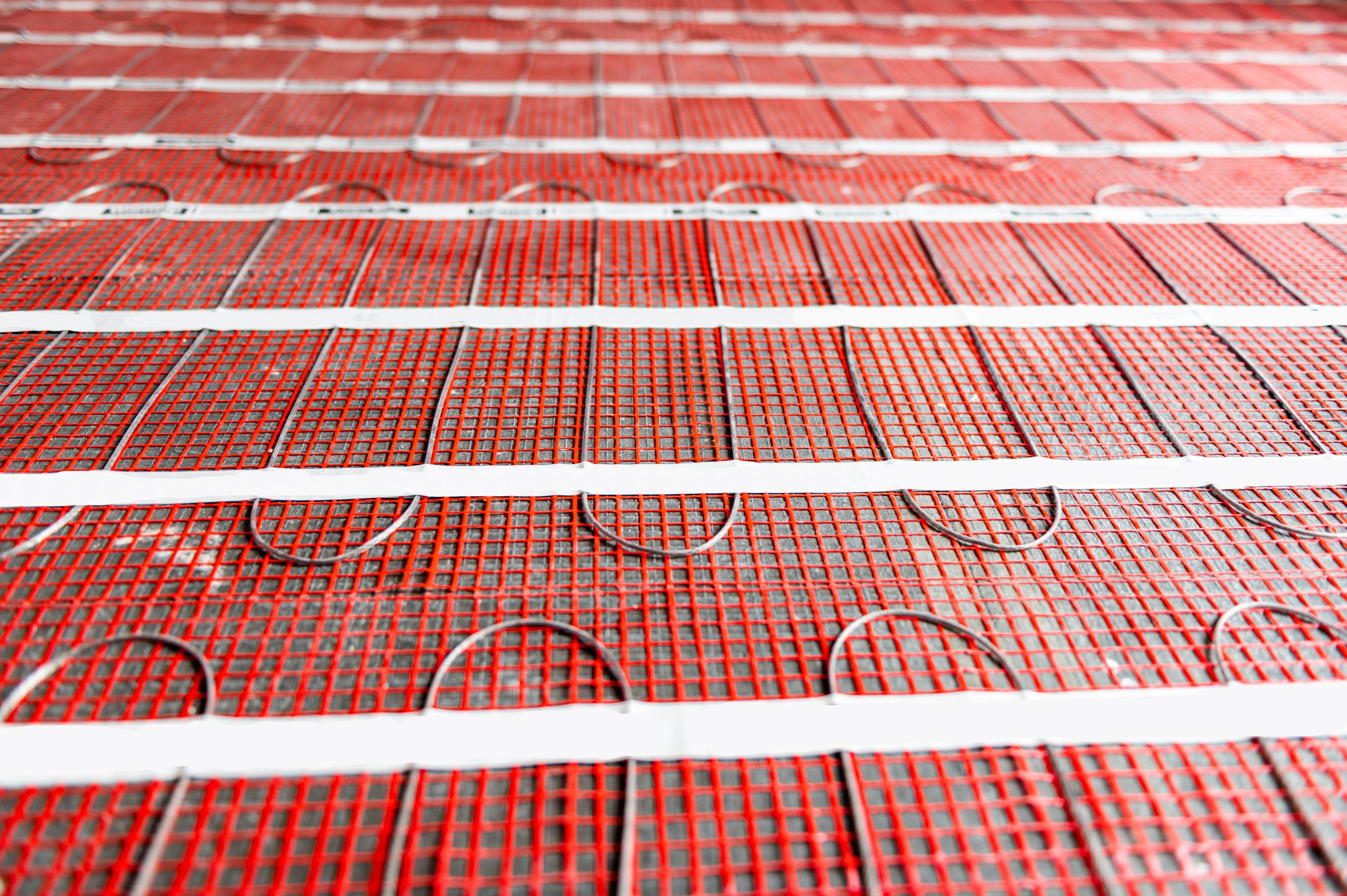 Electric underfloor heating mats laid over a bare subfloor before tile, with the heating cable visible in the mesh