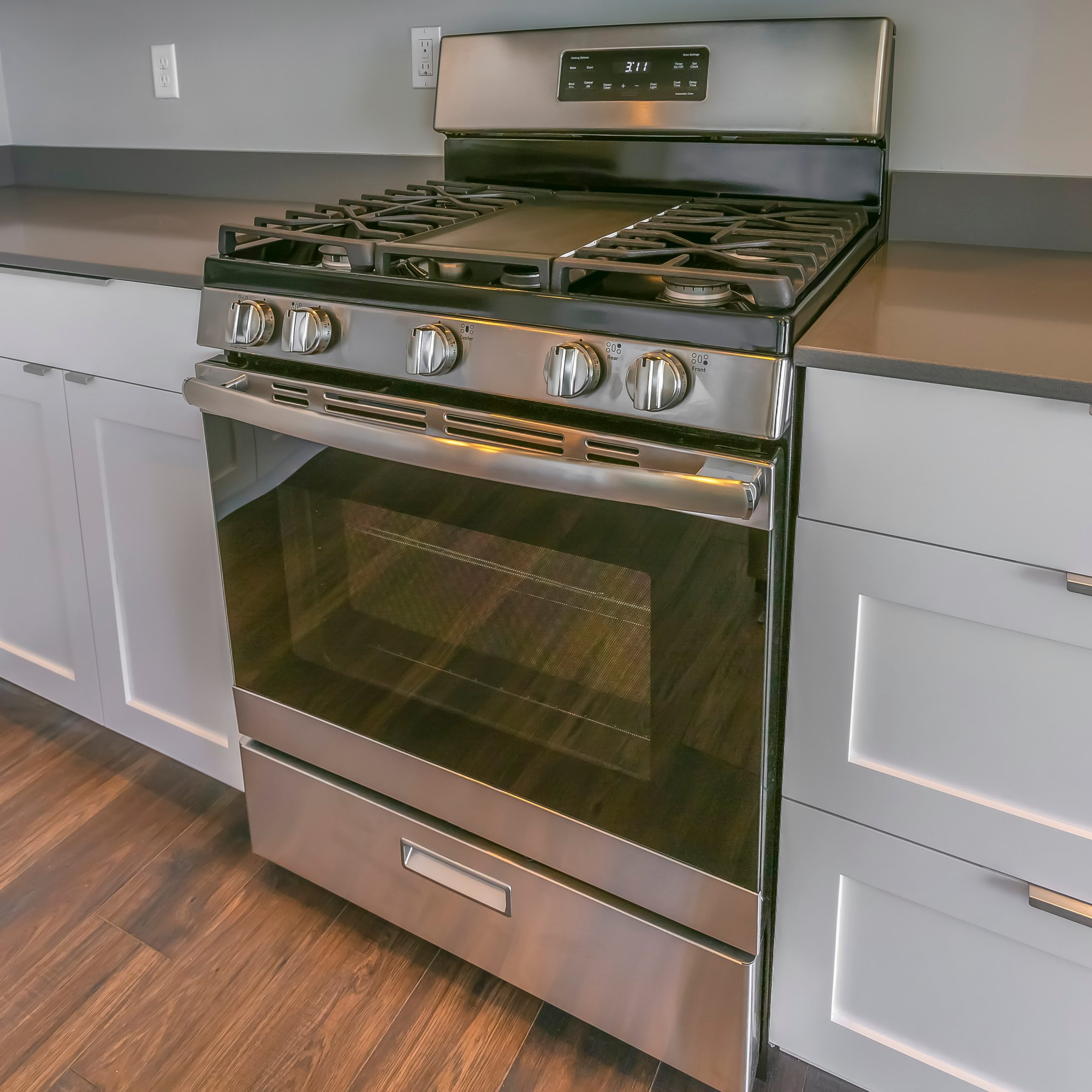 Stainless freestanding gas range with a rear control backguard installed between white cabinets and quartz countertops