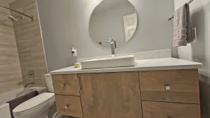 Wood-grain bathroom vanity with a rectangular vessel sink and round mirror
