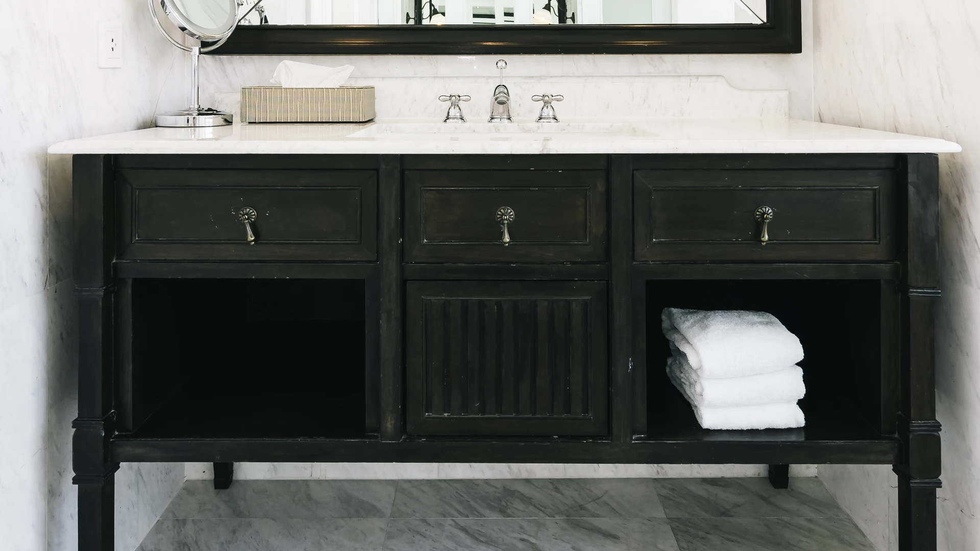 Black furniture-style bathroom vanity with a light countertop, open shelves and folded white towels