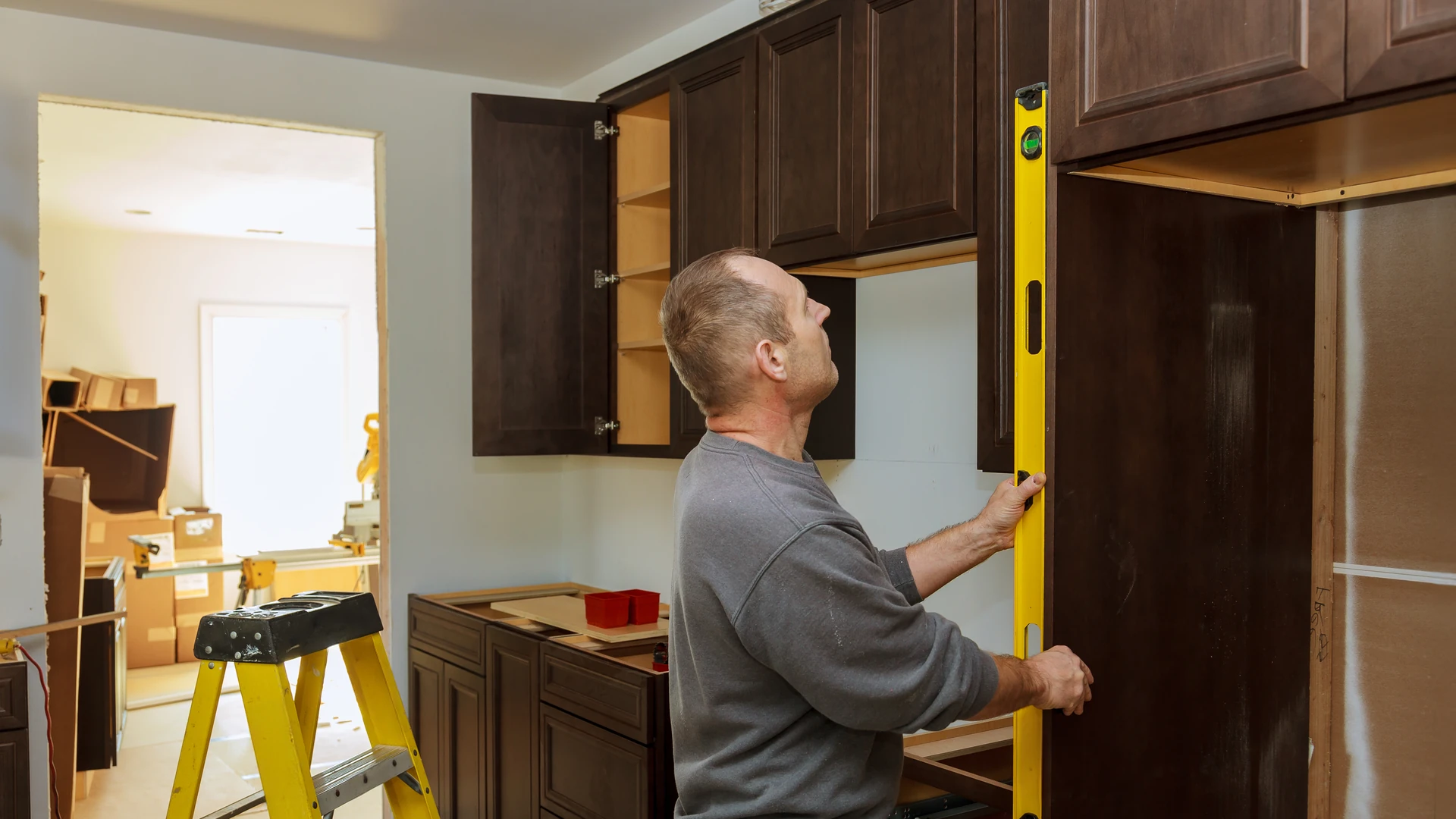 Person holding a yellow level against dark kitchen cabinets during construction