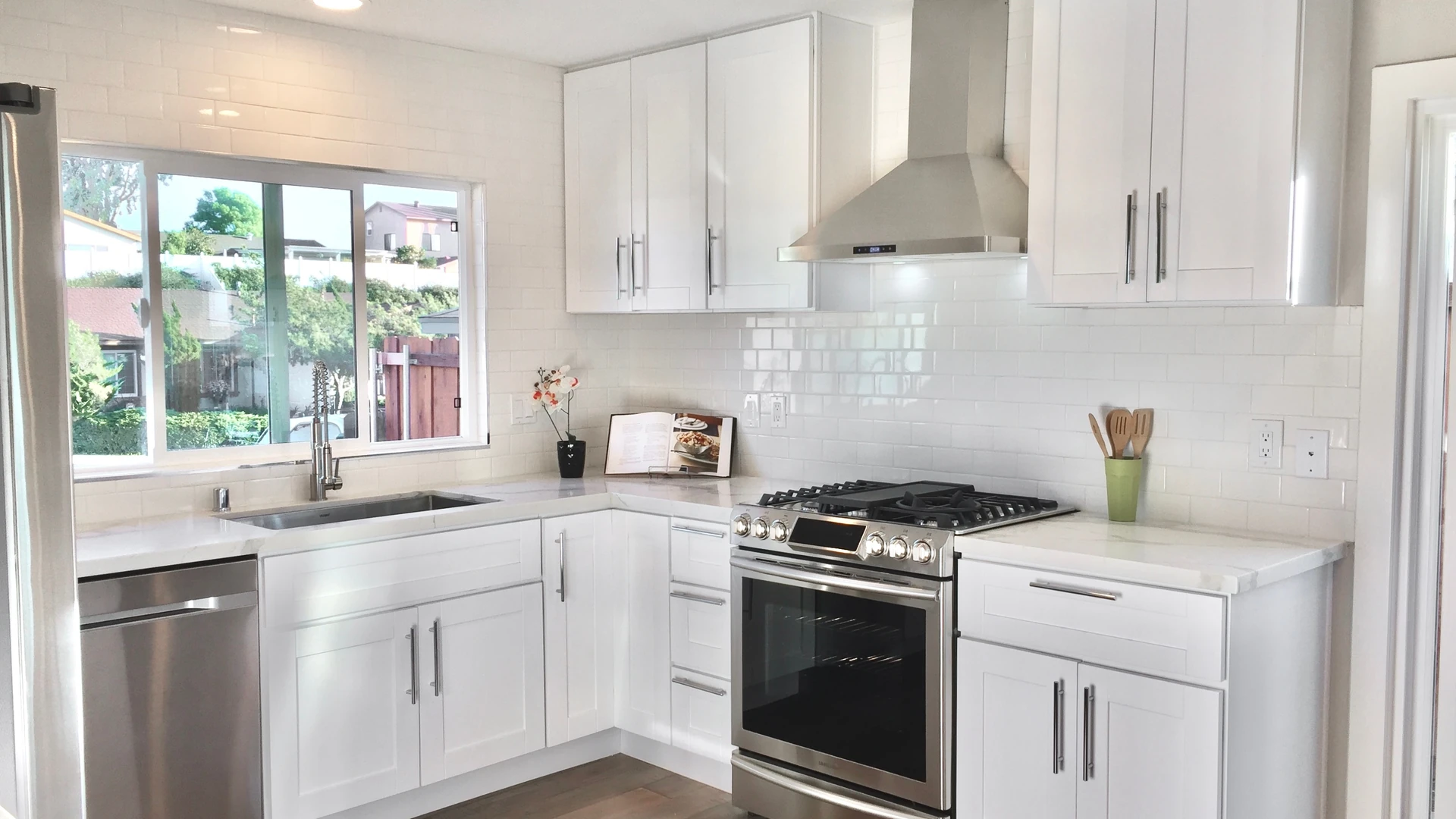 Bright white shaker kitchen with subway tile, a stainless range and hood, and a sink beneath a window