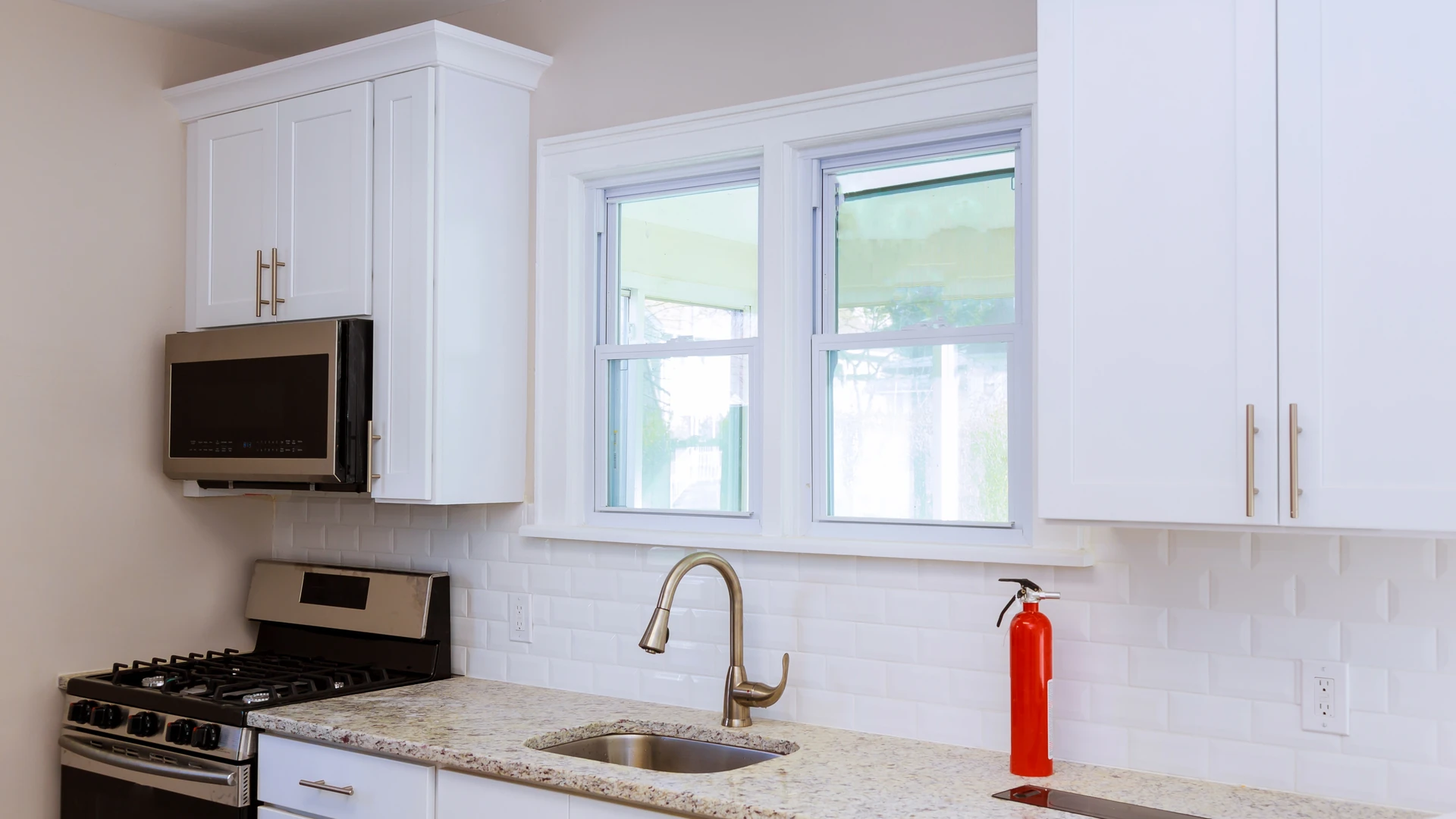 Small white kitchen with a double window over the sink between shaker upper cabinets, a gas range and an over-the-range microwave