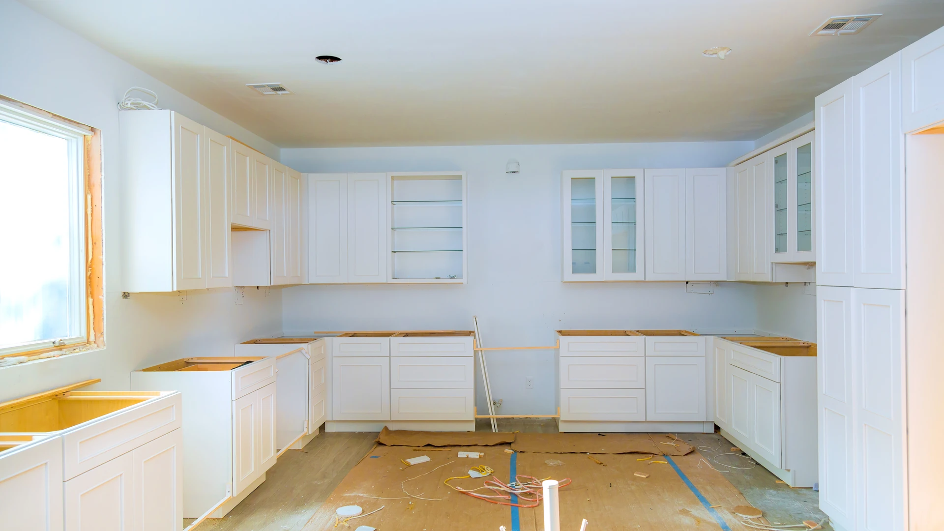 Kitchen under construction with white cabinets, unfinished counters and exposed floor connections