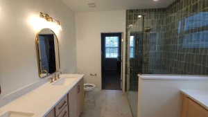 Bathroom with a glass-enclosed shower walled in green rectangular tile, a white veined tile floor and a double vanity