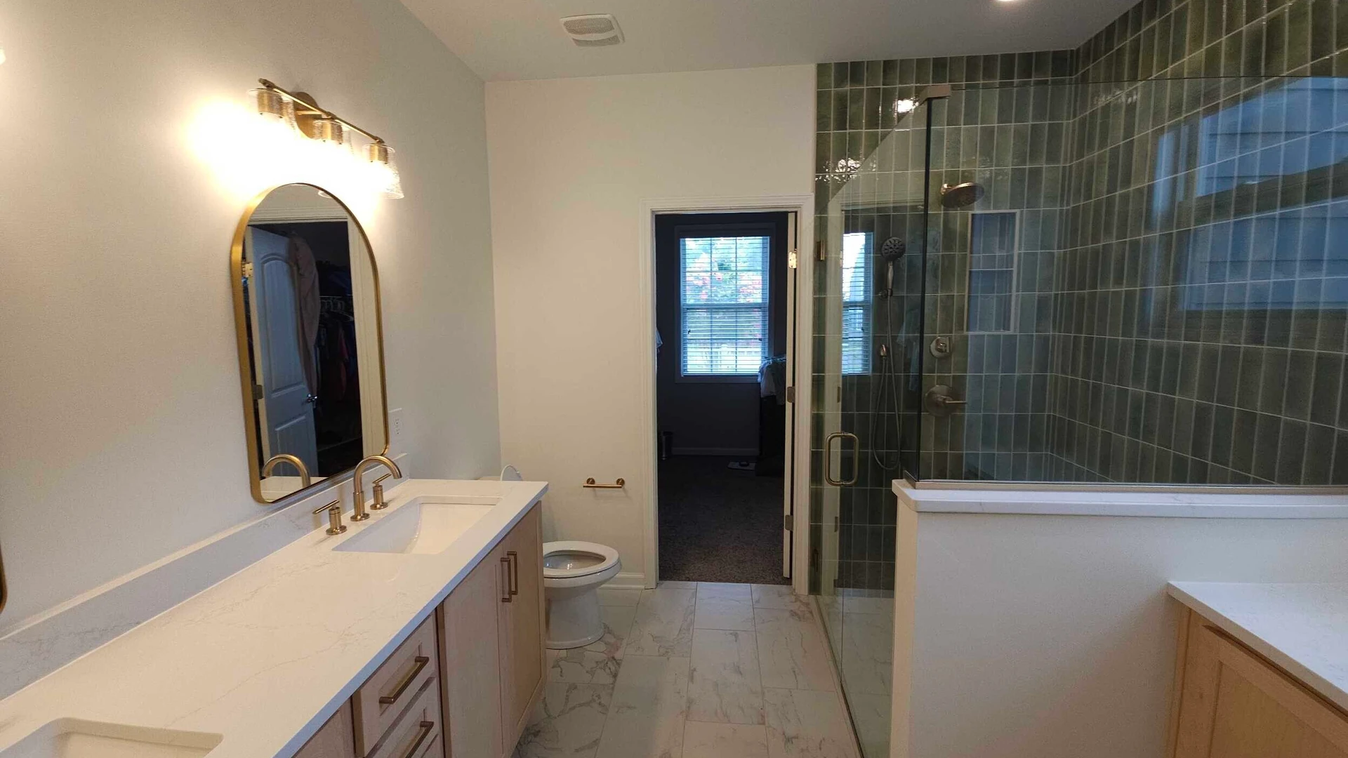 Bathroom with a glass-enclosed shower walled in green rectangular tile, a white veined tile floor and a double vanity